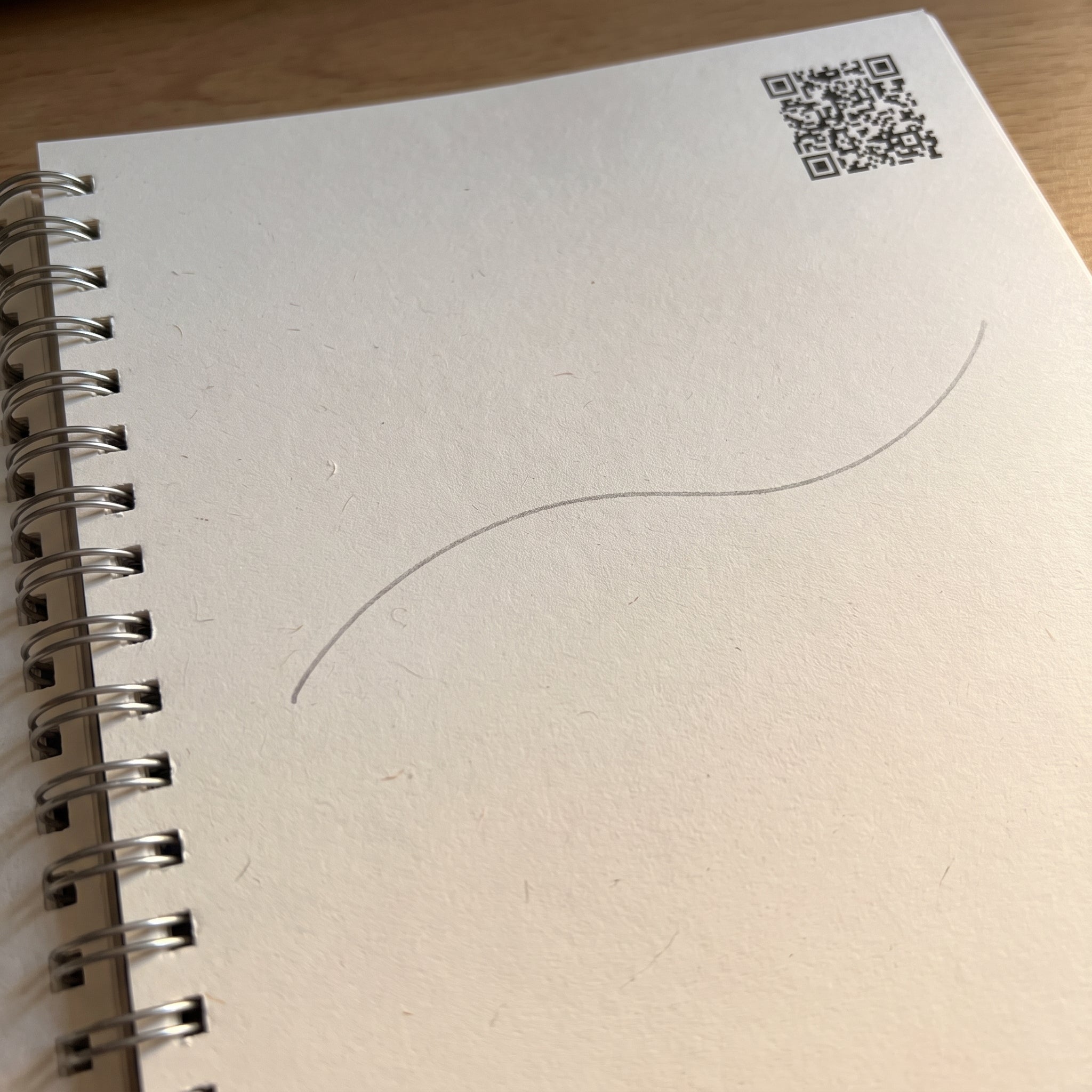 Overhead close-up of a single workbook page with a QR code in the top-right corner and a light grey first-stroke line already printed on it.